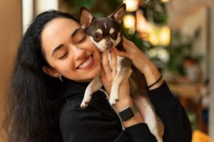 A woman with a smile on her face hugging a small black and tan dog